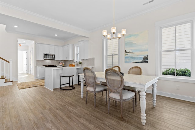 dining area featuring sink, light hardwood / wood-style floors, crown molding, and an inviting chandelier