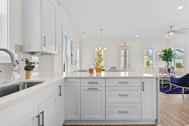 kitchen with open floor plan, a peninsula, light countertops, white cabinetry, and a sink