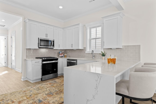 kitchen featuring stainless steel appliances, a peninsula, a kitchen bar, and white cabinets