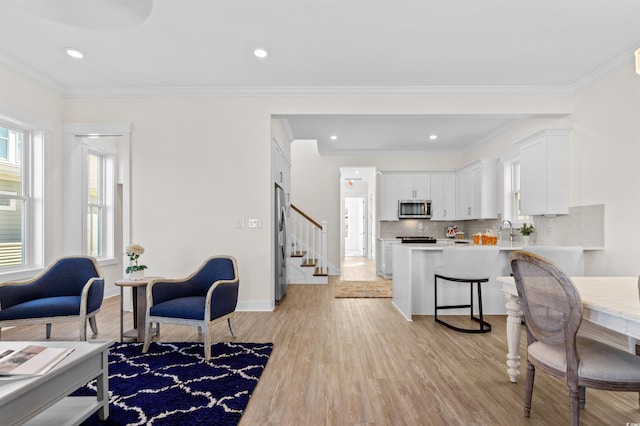 living area featuring light wood finished floors, baseboards, stairs, crown molding, and recessed lighting