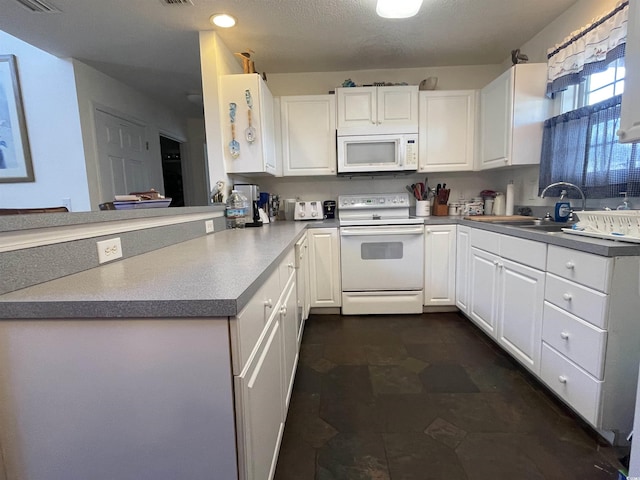 kitchen with a peninsula, white appliances, white cabinets, and a sink