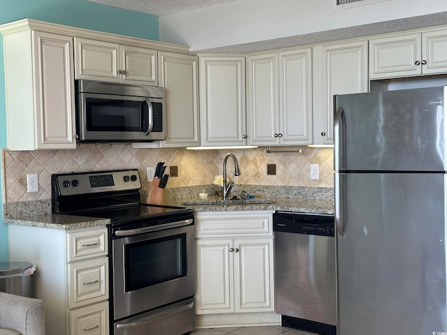 kitchen with cream cabinetry, stainless steel appliances, light stone counters, backsplash, and sink