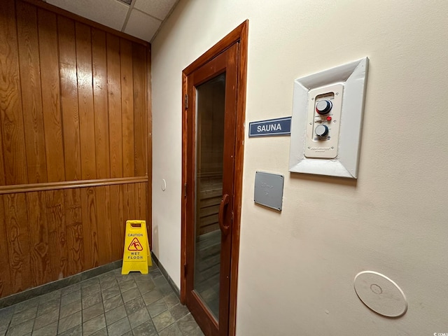 hallway featuring wooden walls, dark tile floors, and a drop ceiling