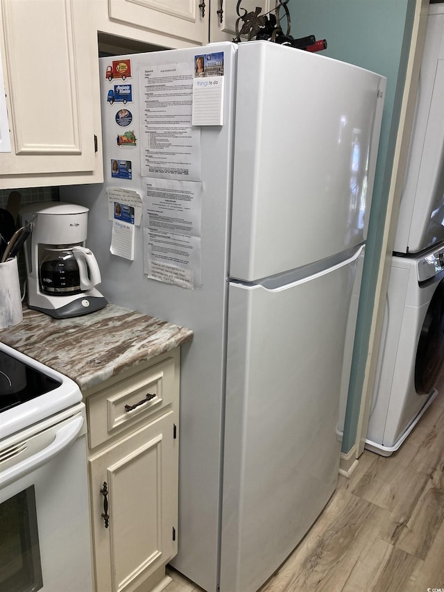 kitchen with light hardwood / wood-style floors, white appliances, and stacked washer and clothes dryer