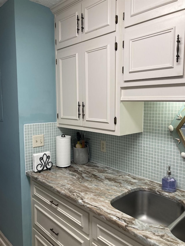 kitchen with white cabinets, light stone countertops, sink, and tasteful backsplash