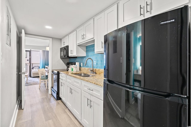 kitchen with white cabinetry, tasteful backsplash, light wood-type flooring, black appliances, and sink