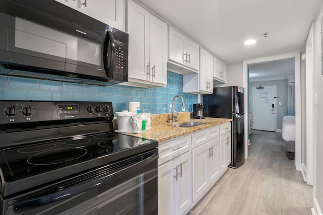 kitchen with white cabinetry, black appliances, light wood-type flooring, light stone counters, and backsplash