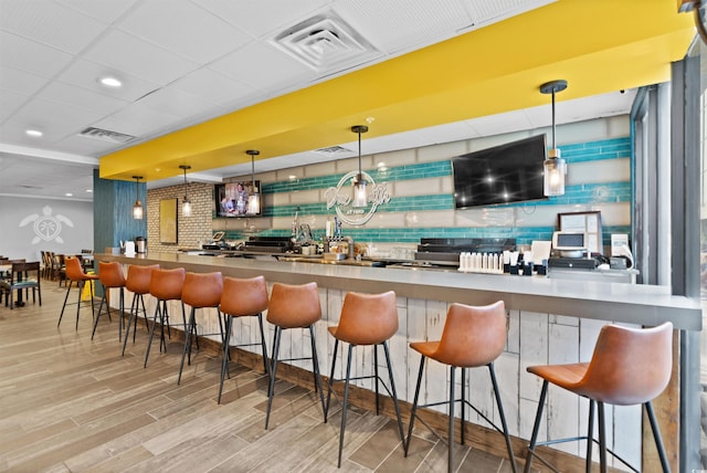 bar featuring a drop ceiling, hanging light fixtures, and light wood-type flooring