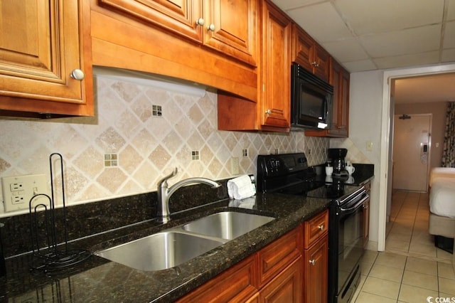 kitchen featuring light tile floors, dark stone countertops, black appliances, a paneled ceiling, and sink