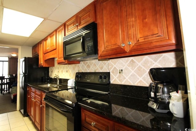 kitchen featuring dark stone counters, light tile floors, black appliances, a paneled ceiling, and sink