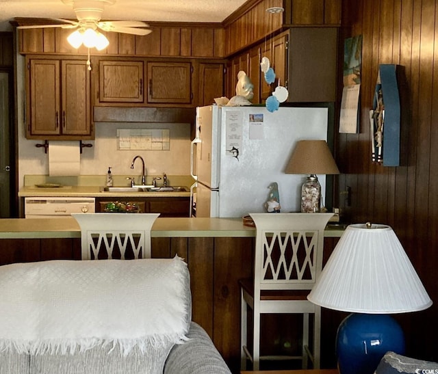 kitchen featuring white appliances, wooden walls, ceiling fan, and sink