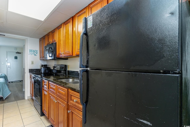 kitchen with dark stone counters, a drop ceiling, black appliances, sink, and light tile floors