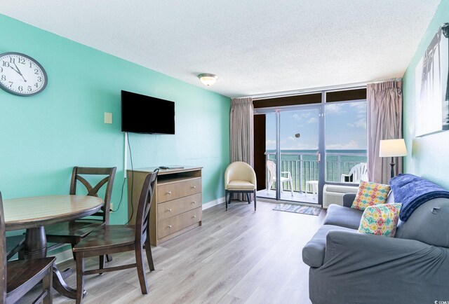 living room featuring a textured ceiling, light wood-type flooring, a water view, and expansive windows