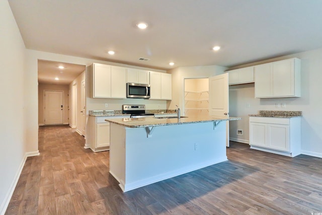 kitchen with appliances with stainless steel finishes, hardwood / wood-style floors, and a center island with sink