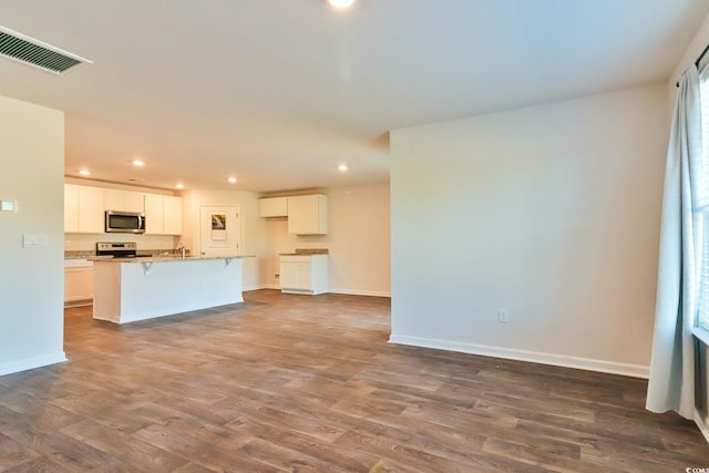 kitchen with a kitchen island with sink, stove, dark hardwood / wood-style flooring, white cabinets, and a breakfast bar