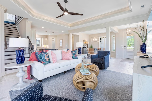 living room featuring ornamental molding, ceiling fan with notable chandelier, a raised ceiling, and decorative columns