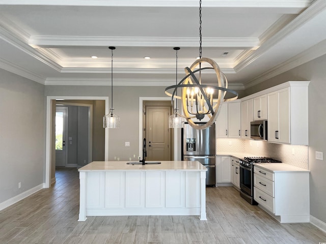 kitchen with appliances with stainless steel finishes, hanging light fixtures, a kitchen island with sink, sink, and a raised ceiling