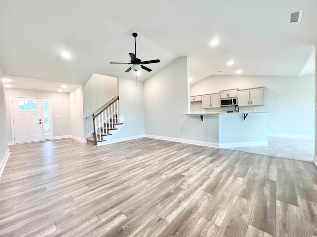 unfurnished living room featuring ceiling fan, vaulted ceiling, and light wood-type flooring