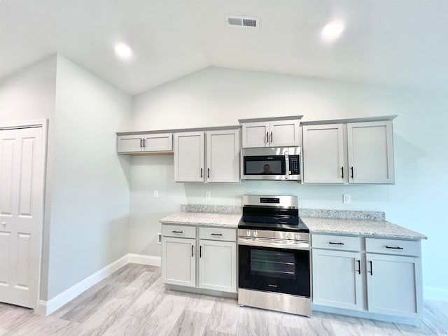 kitchen featuring vaulted ceiling, light stone counters, stainless steel appliances, and light hardwood / wood-style floors