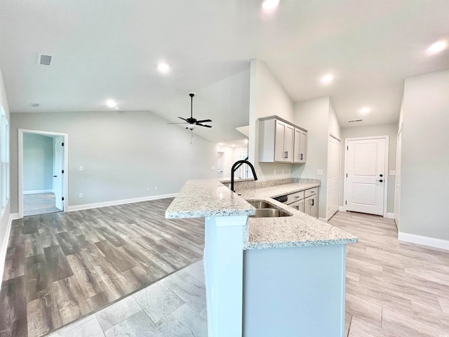 kitchen with lofted ceiling, kitchen peninsula, ceiling fan, light hardwood / wood-style flooring, and sink