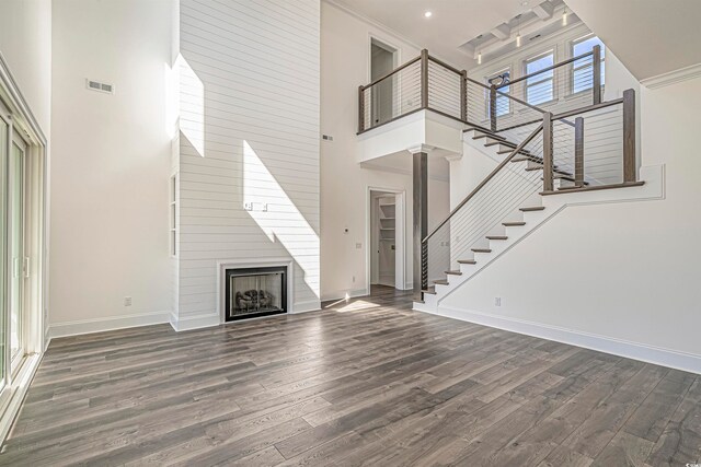 unfurnished living room with a towering ceiling, dark hardwood / wood-style floors, a large fireplace, and ornamental molding