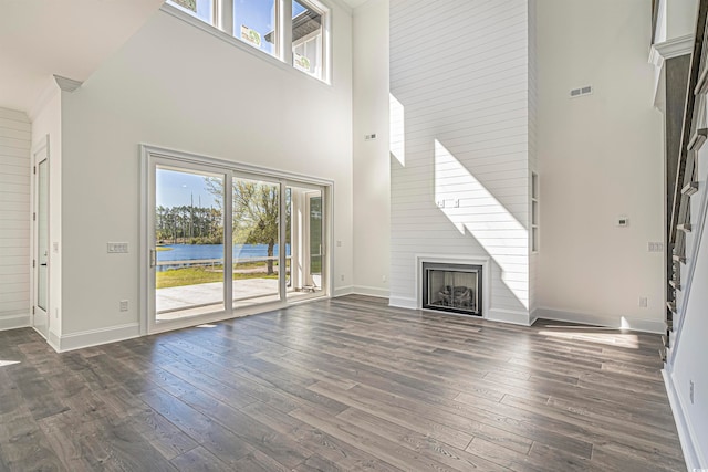 unfurnished living room with dark wood-type flooring, a water view, a towering ceiling, and a fireplace