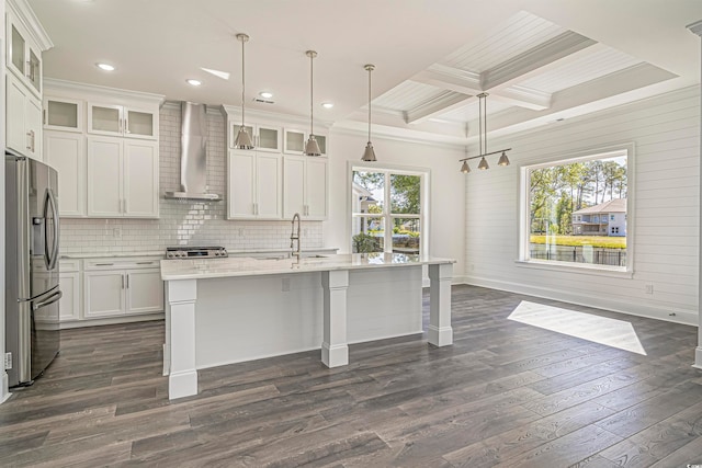 kitchen with an island with sink, appliances with stainless steel finishes, dark hardwood / wood-style floors, wall chimney exhaust hood, and decorative light fixtures