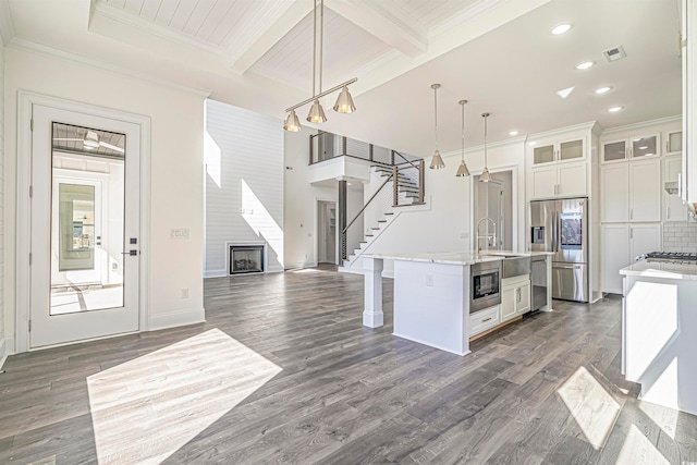 kitchen featuring dark hardwood / wood-style flooring, appliances with stainless steel finishes, an island with sink, white cabinetry, and decorative light fixtures