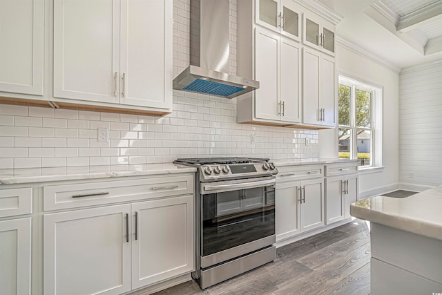 kitchen with wall chimney range hood, white cabinetry, stainless steel stove, crown molding, and hardwood / wood-style flooring