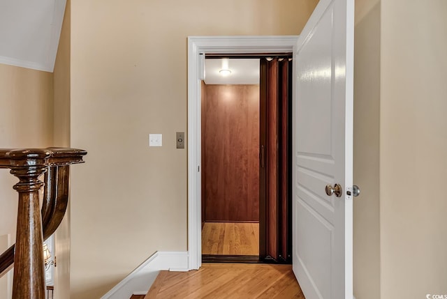 hall with light hardwood / wood-style floors, ornamental molding, and elevator