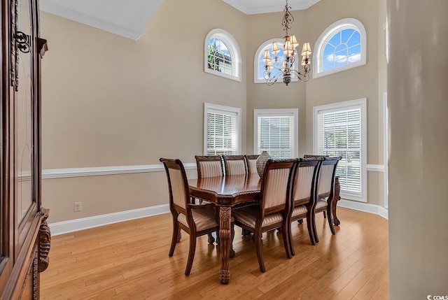 dining room with a towering ceiling, crown molding, a chandelier, and light wood-type flooring