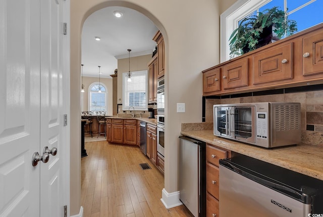 kitchen featuring pendant lighting, ornamental molding, appliances with stainless steel finishes, tasteful backsplash, and light wood-type flooring