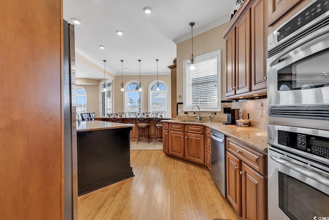 kitchen with tasteful backsplash, hanging light fixtures, light hardwood / wood-style flooring, light stone countertops, and sink