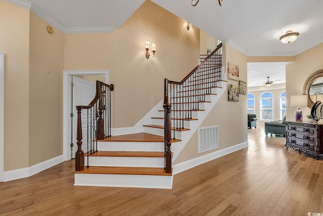 stairway with ceiling fan, crown molding, and light wood-type flooring