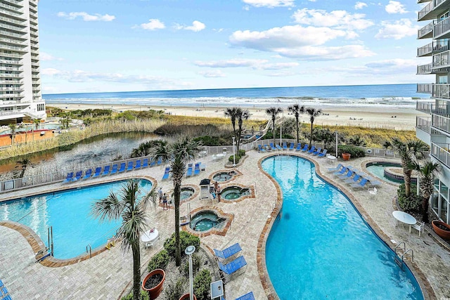 view of swimming pool featuring a patio, a community hot tub, a water view, and a view of the beach