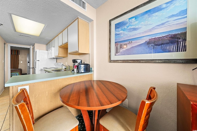 interior space with light tile patterned floors, kitchen peninsula, a textured ceiling, range, and a kitchen breakfast bar