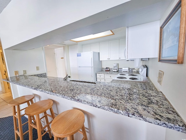 kitchen featuring white fridge, kitchen peninsula, dark stone countertops, tile floors, and a breakfast bar