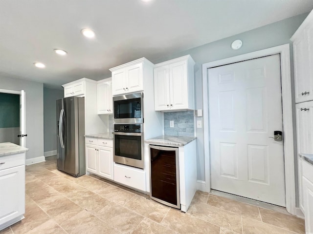 kitchen featuring appliances with stainless steel finishes, backsplash, light tile floors, light stone countertops, and white cabinets