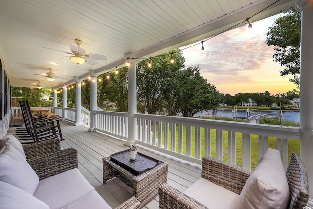 deck at dusk with a water view, an outdoor hangout area, and ceiling fan