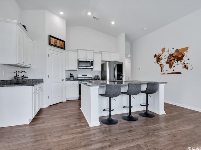 kitchen with a kitchen bar, appliances with stainless steel finishes, dark wood-type flooring, a kitchen island with sink, and white cabinets