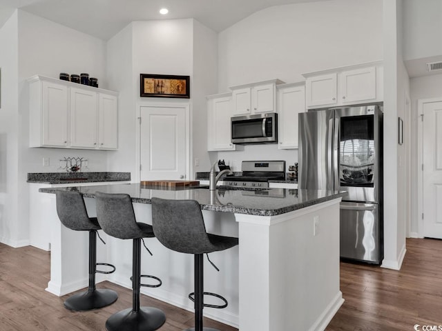 kitchen featuring appliances with stainless steel finishes, dark wood-type flooring, an island with sink, white cabinetry, and a breakfast bar