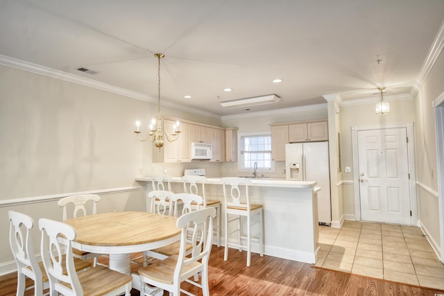 dining area with sink, light hardwood / wood-style floors, an inviting chandelier, and crown molding