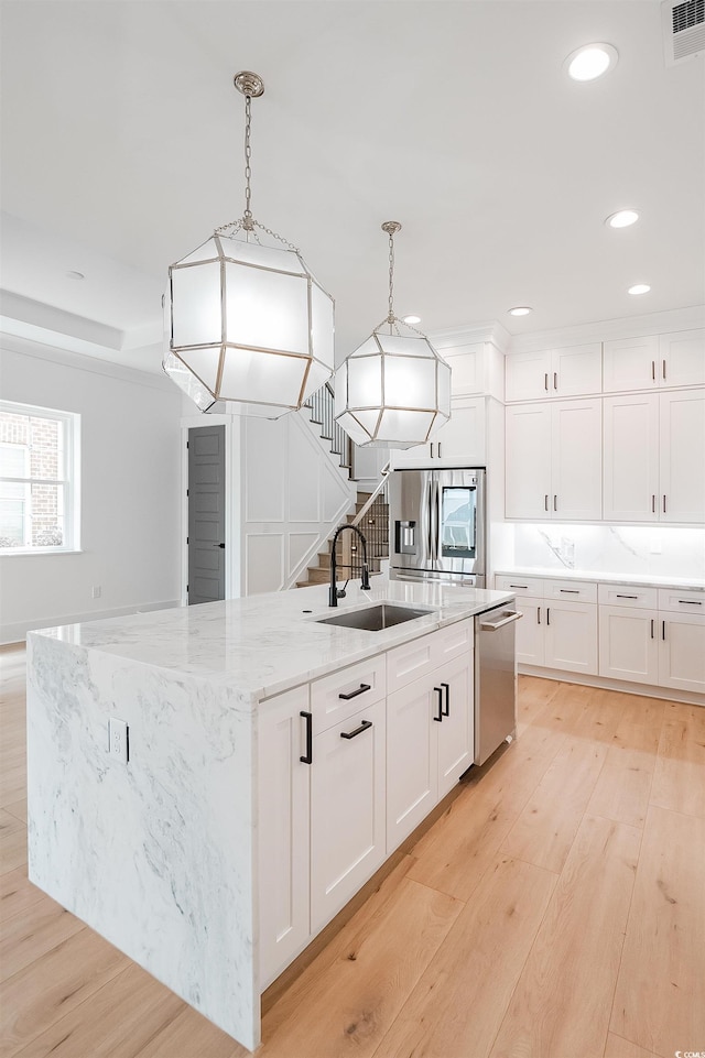 kitchen featuring hanging light fixtures, stainless steel appliances, a kitchen island with sink, white cabinets, and light wood-type flooring