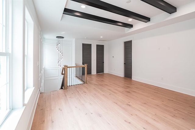 empty room with beam ceiling and light hardwood / wood-style floors