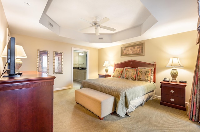 carpeted bedroom featuring a raised ceiling, ensuite bathroom, and ceiling fan