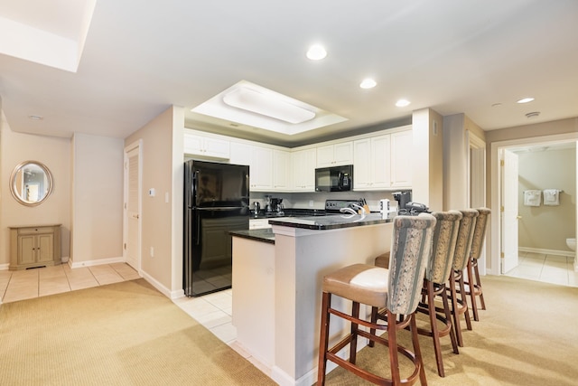 kitchen featuring a breakfast bar area, black appliances, kitchen peninsula, light colored carpet, and white cabinetry