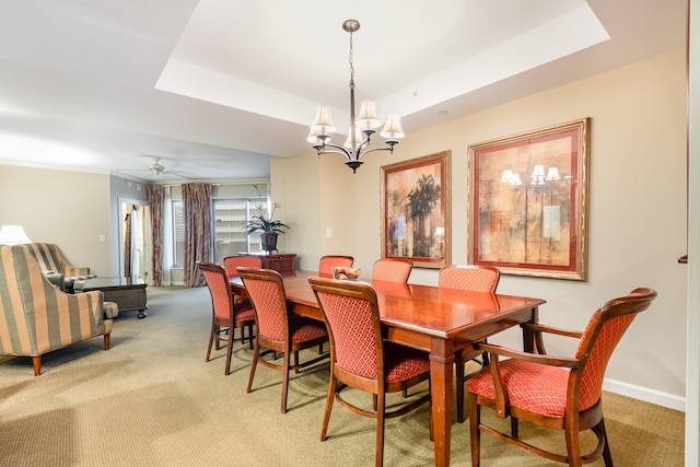 dining area with carpet floors, ceiling fan with notable chandelier, and a tray ceiling