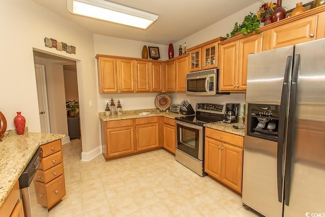 kitchen with light tile flooring, appliances with stainless steel finishes, and light stone counters