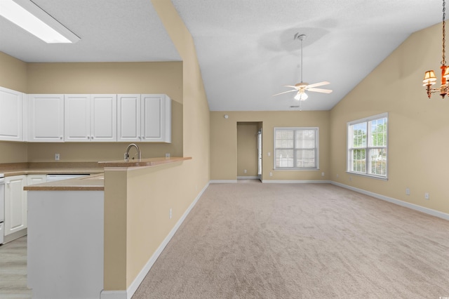 kitchen featuring light colored carpet, ceiling fan with notable chandelier, lofted ceiling, white cabinetry, and pendant lighting