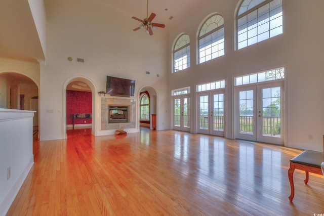 unfurnished living room with ceiling fan, a multi sided fireplace, light wood-type flooring, and a high ceiling